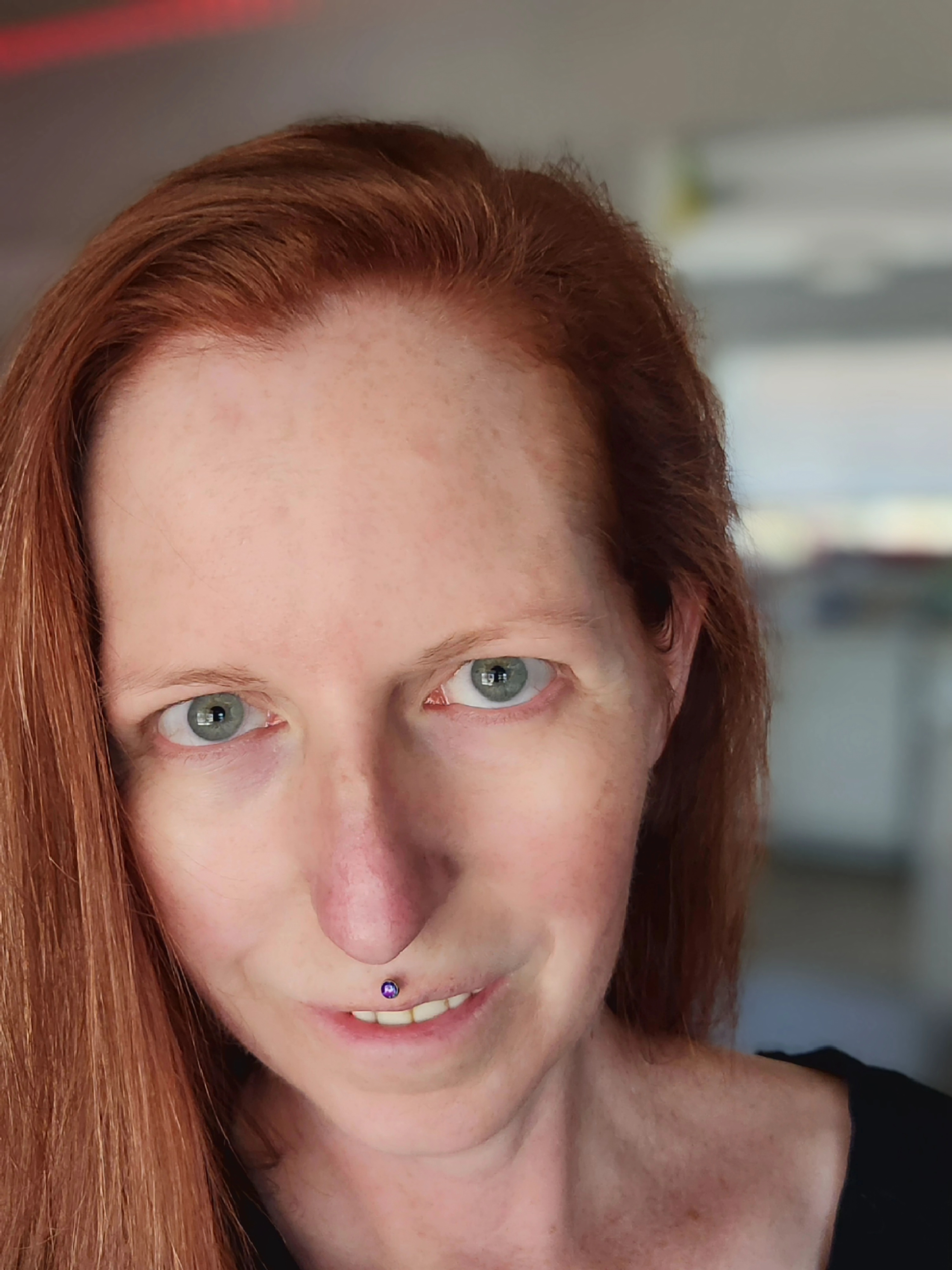 portrait of a woman with red hair, green eyes, and a purple opal medusa piercing staring directly at the camera